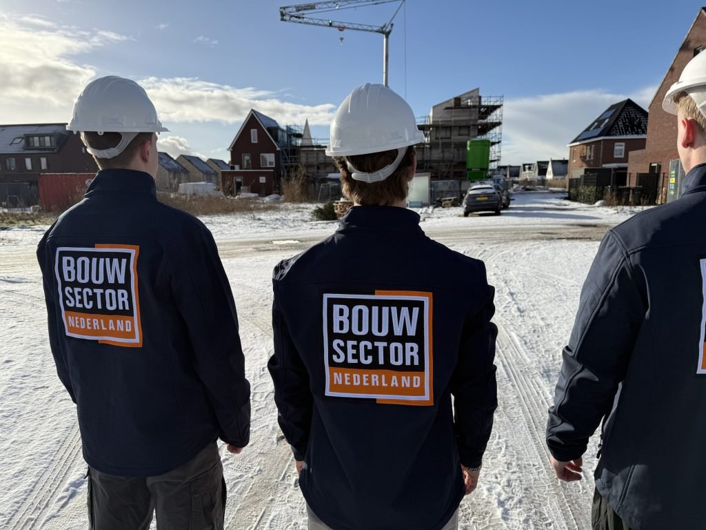 Drie vakmensen van Bouwsector Nederland met witte helm op een besneeuwde nieuwbouwstraat